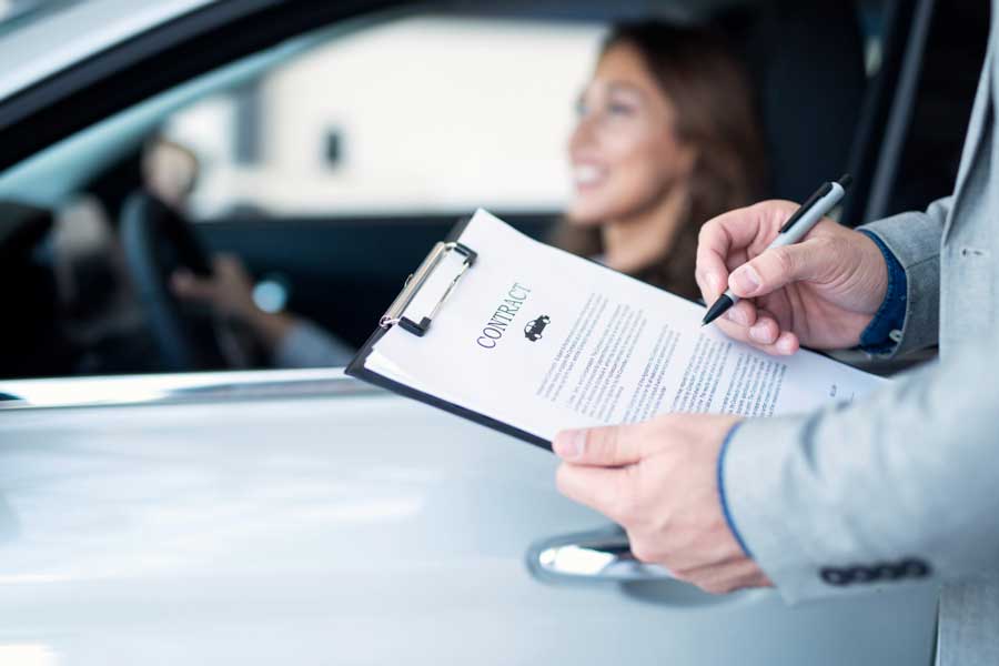 Appraisal Clause Auto Insurance process showing an insurance agent reviewing and signing a vehicle contract while a driver sits in the car, representing auto insurance claim evaluation and policy agreement.