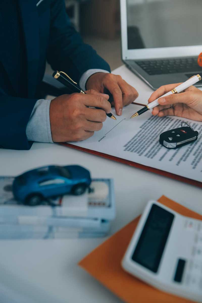 Appraisal Clause Auto Insurance agreement showing two professionals signing an auto insurance document with car keys and a model vehicle on the desk, representing the vehicle appraisal and insurance claim settlement process.