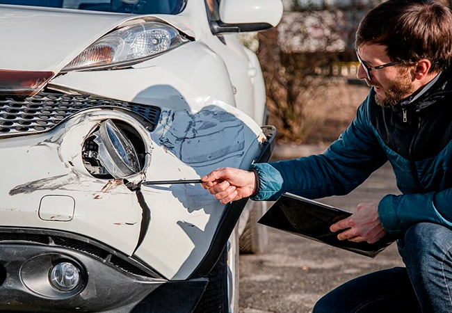 Insurance inspector examining cracked front bumper and headlight damage on a white vehicle, documenting loss for claim processing and Diminished Value Claim California after a car accident