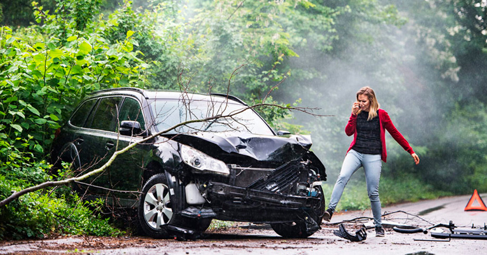 Single-vehicle accident with a damaged SUV off the road among trees as a driver makes a phone call, showing crash aftermath and insurance evaluation for Diminished Value Claim Kansas.