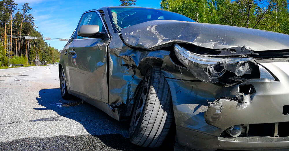 Severely damaged sedan with crushed front and side panels stopped on a roadway after a major collision, illustrating insurance assessment and Total Loss Threshold California following a serious auto accident