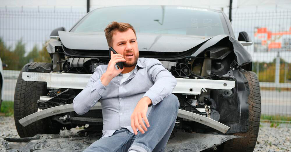 Driver sitting in front of a severely damaged vehicle while speaking on a phone after a major collision, illustrating insurance assessment and Total Loss Threshold Colorado following a serious auto accident