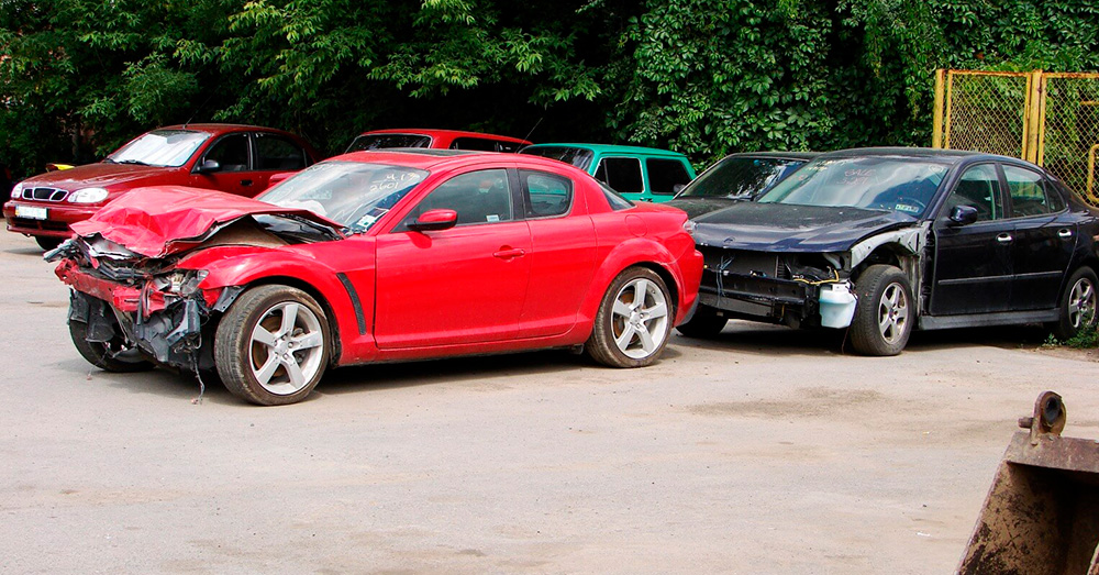 Salvage yard with multiple wrecked vehicles including a red sports car with severe front-end damage, illustrating insurance write-off evaluation and Kansas Total Loss Threshold after major auto accidents.