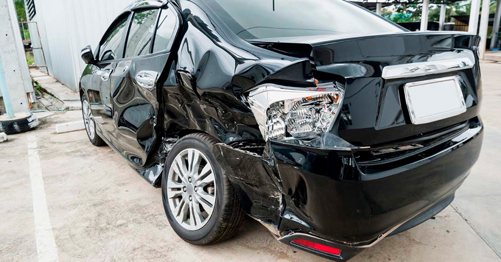 Black sedan with severe rear and side impact damage parked after a collision, representing insurance damage assessment and Total Loss Threshold Maine following an auto accident