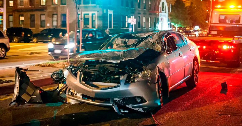 Heavily damaged sedan at a nighttime city intersection with emergency lights and debris after a serious crash, illustrating insurance evaluation and Maryland Total Loss Threshold following a major auto accident