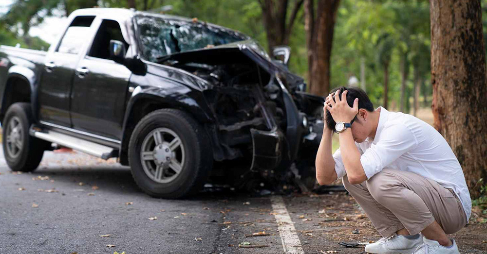 Distressed driver crouching beside a heavily damaged pickup truck after a roadside crash, showing accident aftermath, insurance evaluation, and Mississippi Total Loss Threshold Claim following a severe collision