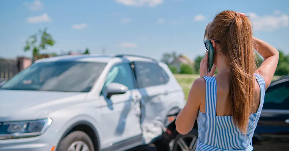Woman on the phone at a car accident scene with visible side-impact damage on an SUV, showing insurance evaluation and Missouri Total Loss Threshold after an auto collision