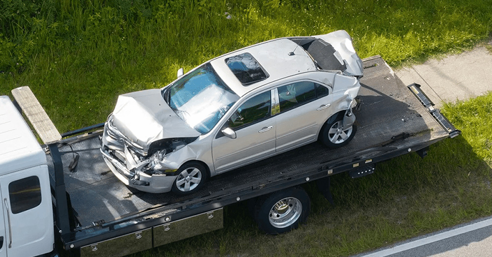 Severely damaged sedan being transported on a flatbed tow truck after a major crash, illustrating insurance evaluation and Nebraska Total Loss Threshold Claim following an auto accident