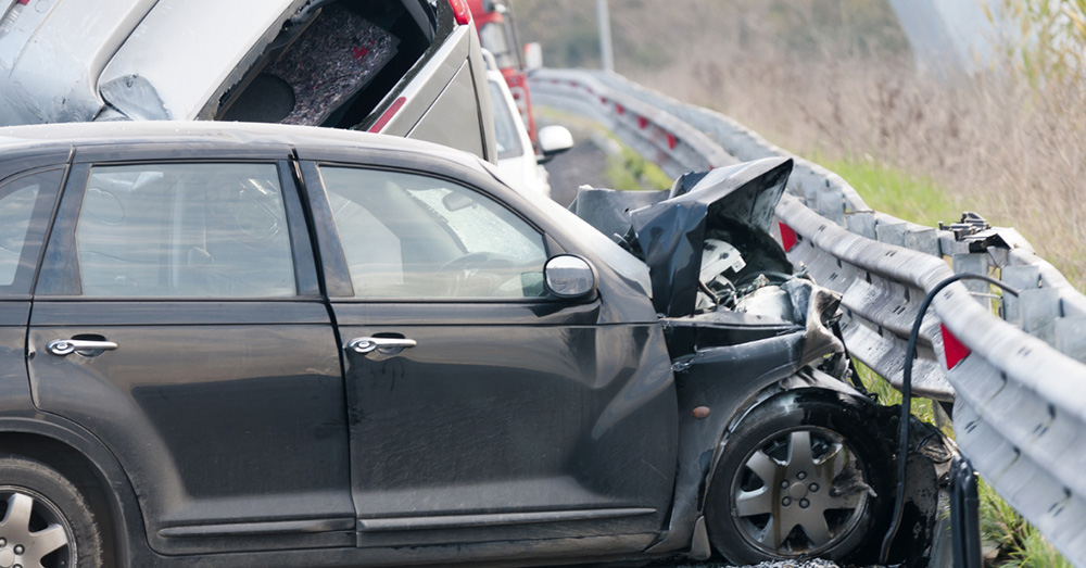 Car crashed into a highway guardrail with extensive side and front damage along a roadway, showing insurance investigation and Pennsylvania Total Loss Threshold after a severe auto accident