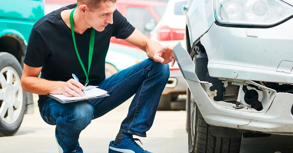 Auto insurance inspector examining bumper damage on a white vehicle while taking notes, illustrating damage assessment and Tennessee Total Loss Threshold after a car accident