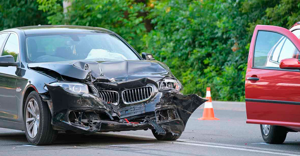 Black luxury sedan with severe front-end damage at a roadside accident scene near traffic cones, representing insurance evaluation and Utah Total Loss Threshold after a major car collision