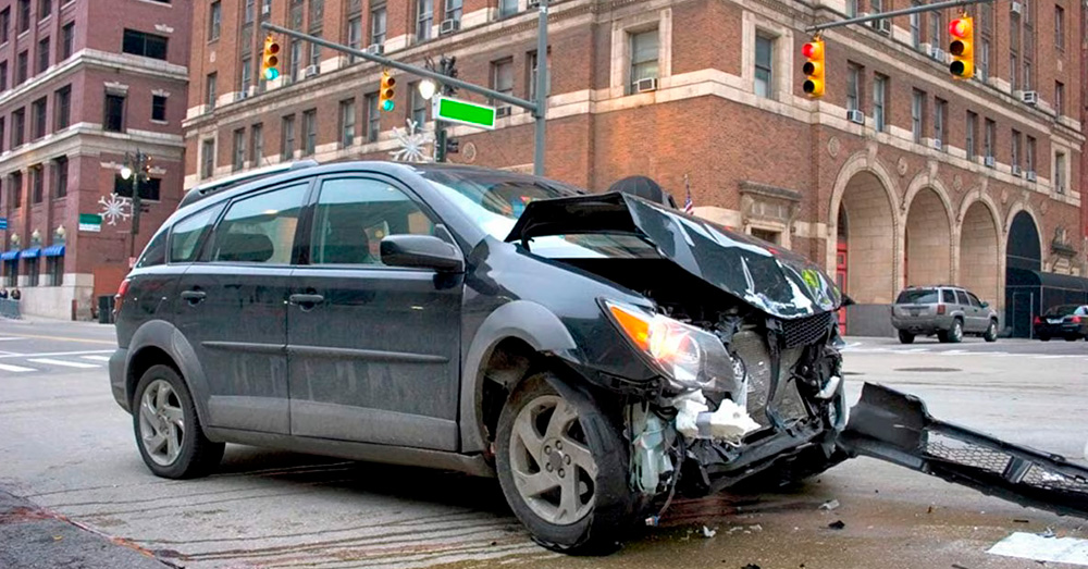 Heavily damaged SUV stopped at a city intersection with front-end collision damage and debris, illustrating insurance assessment and Total Loss Threshold Washington after a serious auto accident.