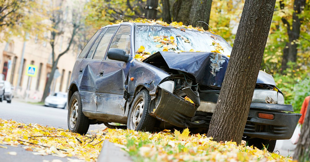 Car crashed into a tree with severe front-end and side damage on a leaf-covered street, illustrating insurance evaluation and Diminished Value Claim South Carolina after a serious auto accident